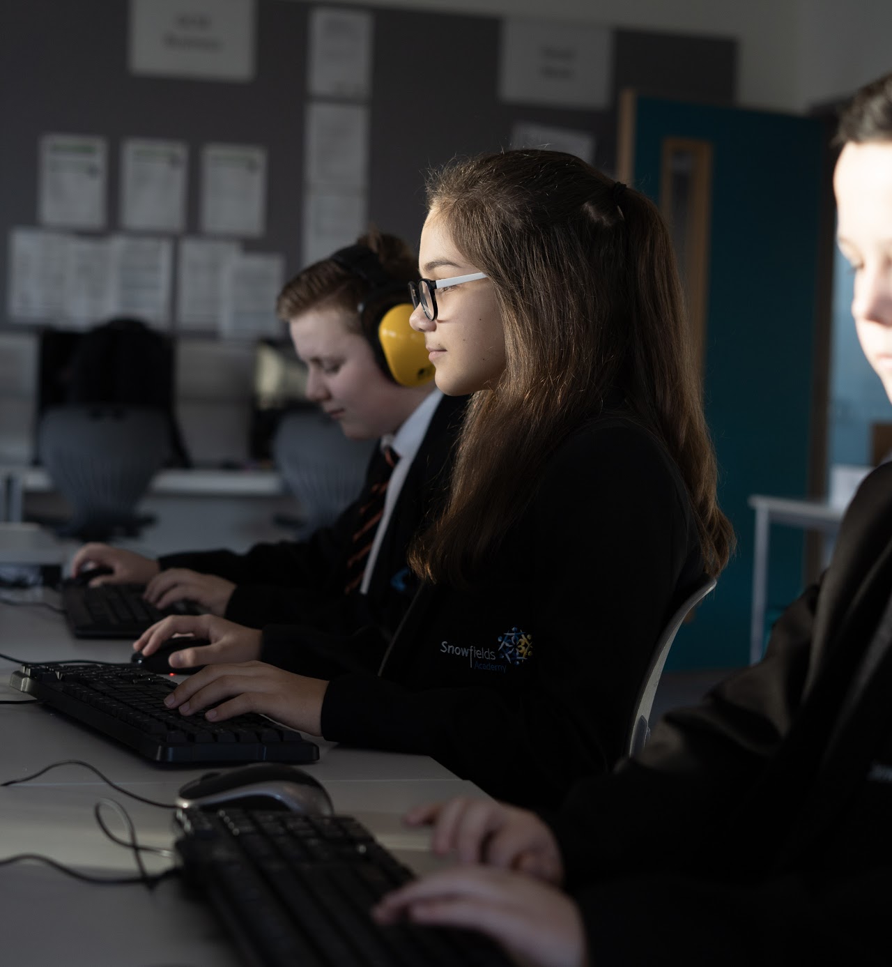 Three children in an IT suite using computers to assist in their learning.