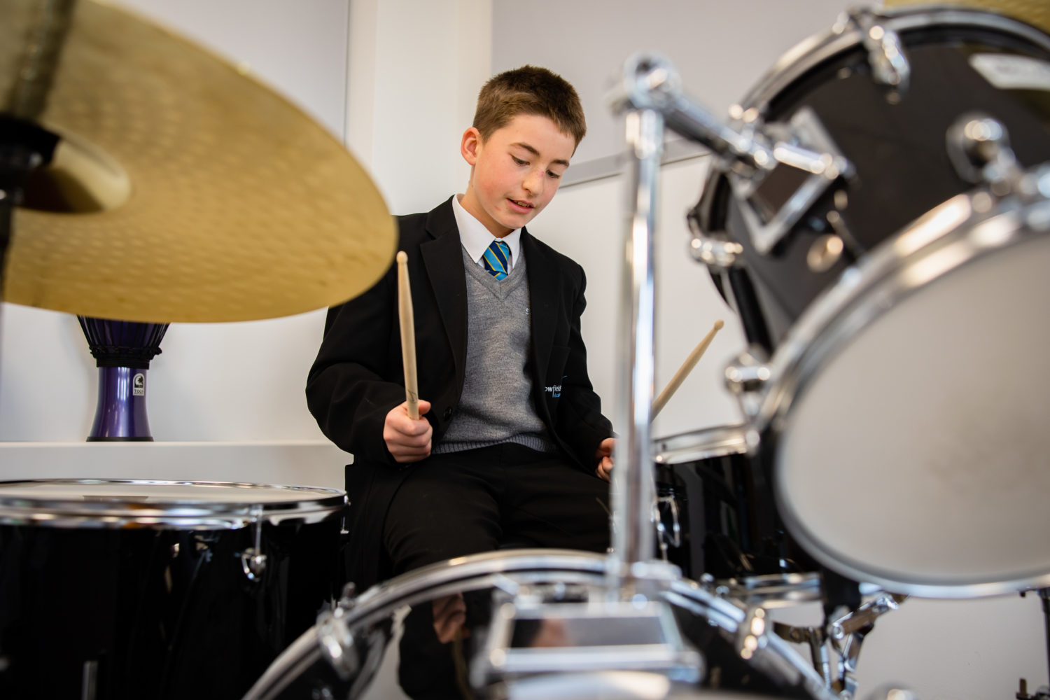 A young boy playing a set of drums in a classroom