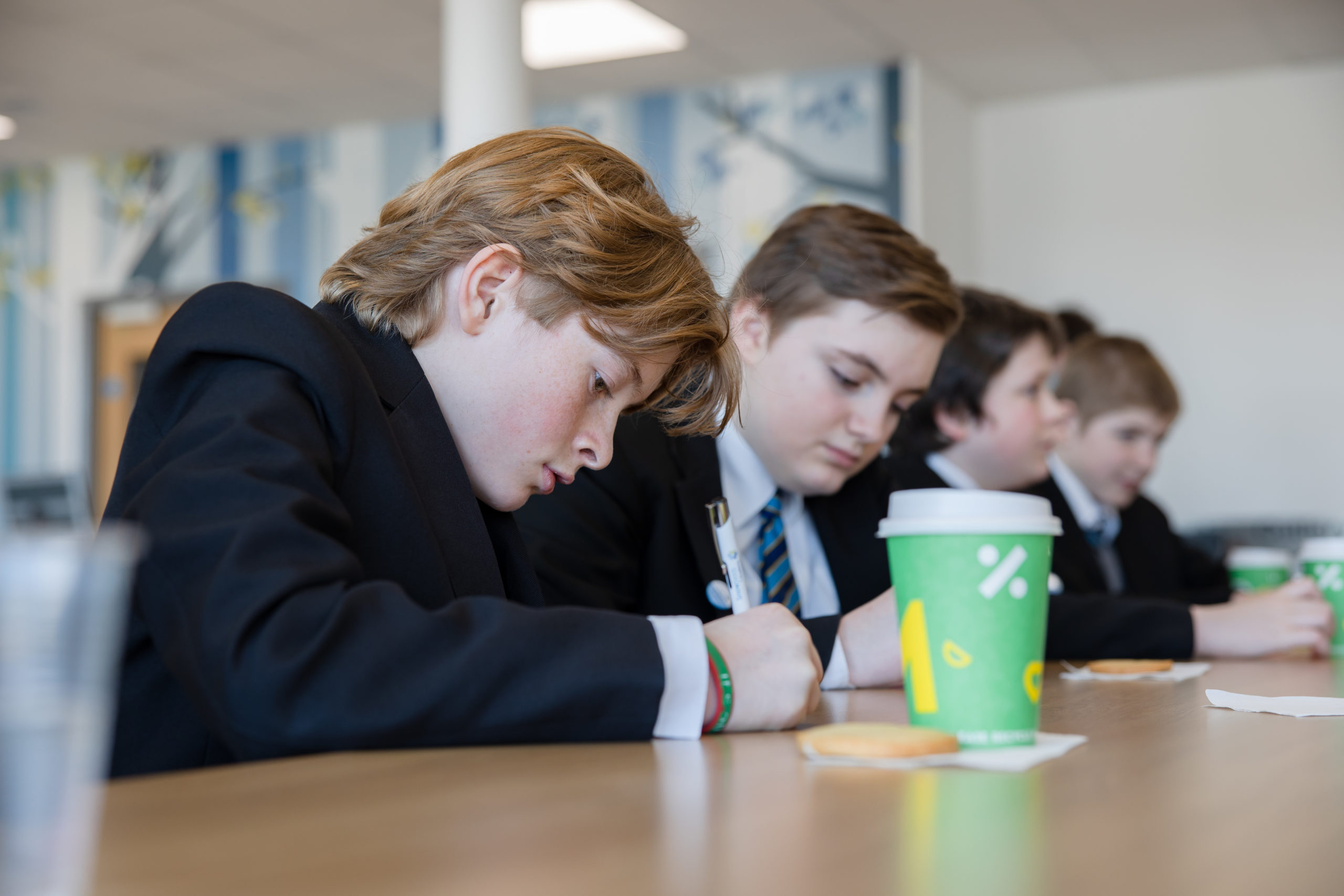 Students sitting on a table writing on a piece of paper with a pen