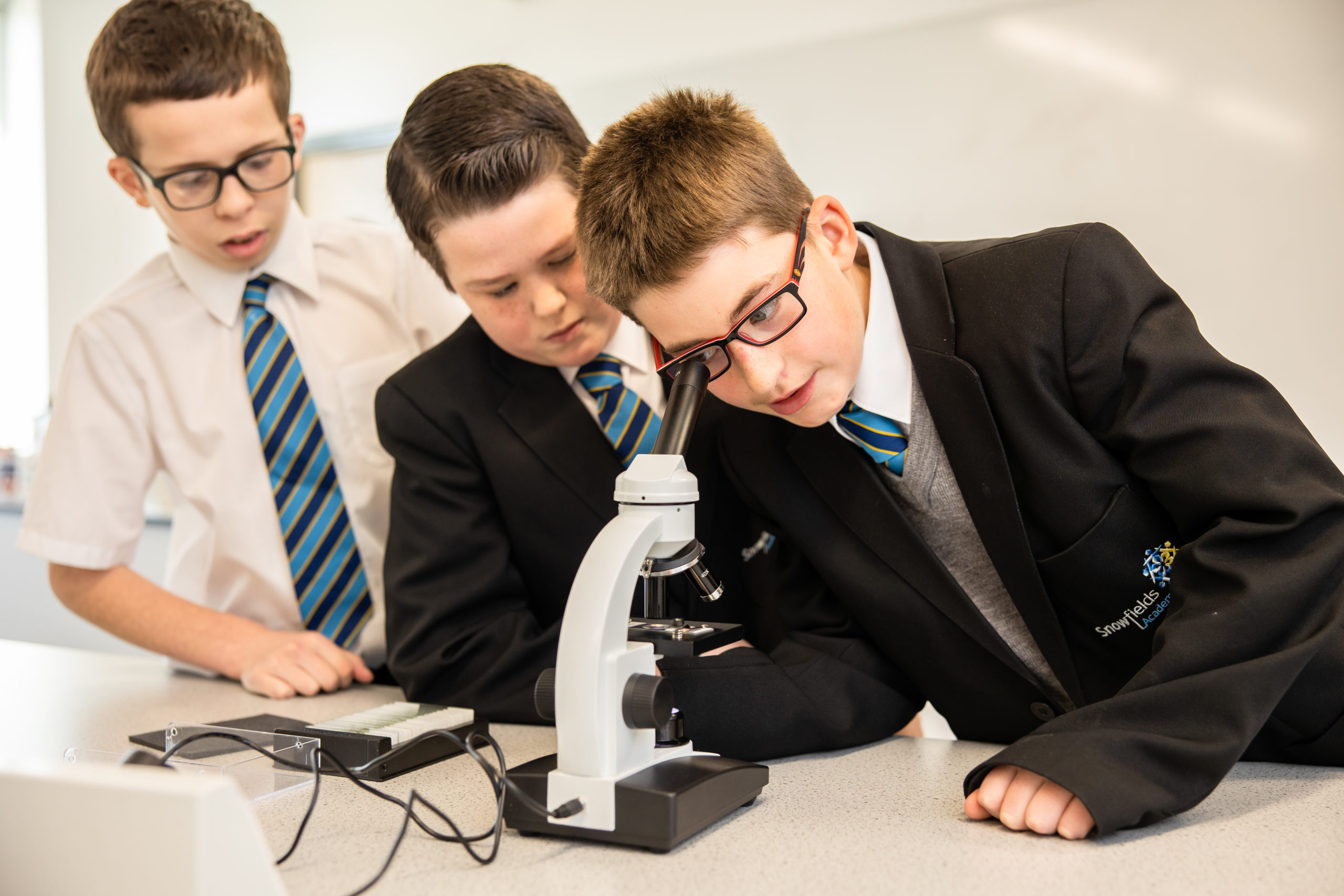 Three students taking in turn to look into a microscope