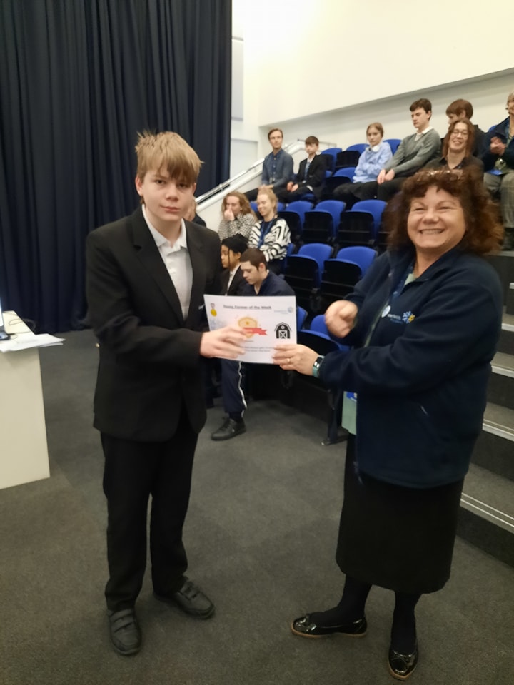 A student is seen posing for a photo for the camera, whilst collecting a certificate he has won from a female member of staff.
