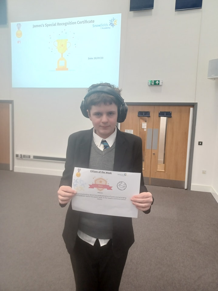 A student can be seen smiling for the camera, whilst holding up a certificate he has won from participating in an activity.
