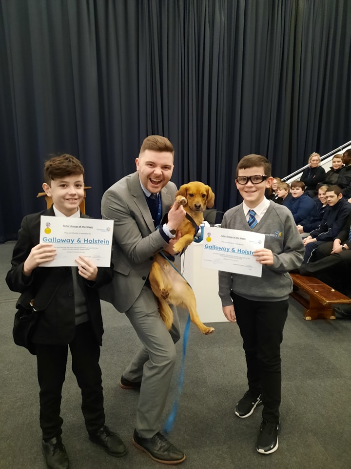 Two Snowfields Academy students are seen posing for a photo alongside a member of staff carrying a pet Dog in his hands.