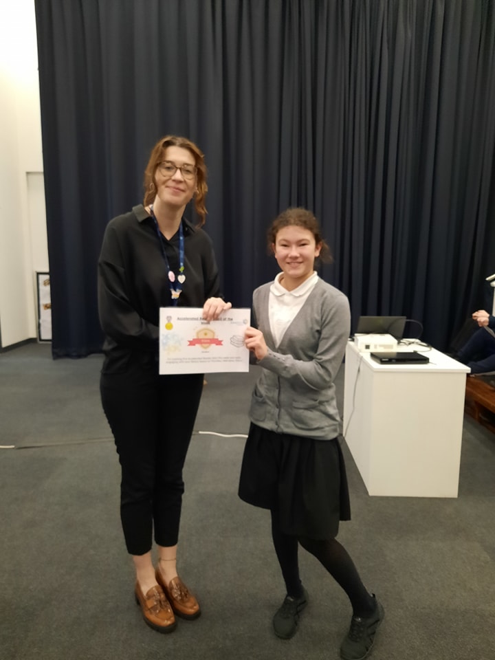 A student is seen posing for a photo for the camera, whilst collecting a certificate she has won from a female member of staff.