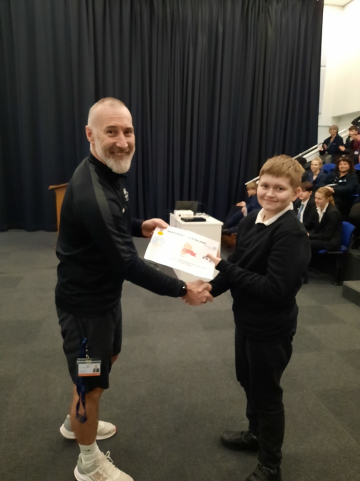 A teenage boy is shown being presented with a certificate he has won by a member of staff.