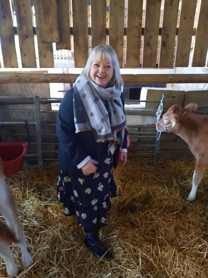 A female member of staff is shown smiling for the camera whilst standing next to a Calf within a farm barn.