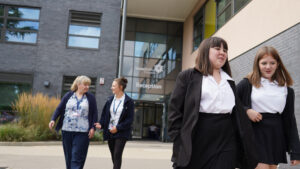Two female students are shown walking together outside the academy building, just ahead of two female staff members behind them chatting with one another.