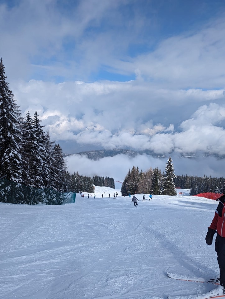 A snowy landscape is pictured with trees and mountains visible. Some Snowfields Academy students can be seen skiing down a hillside.