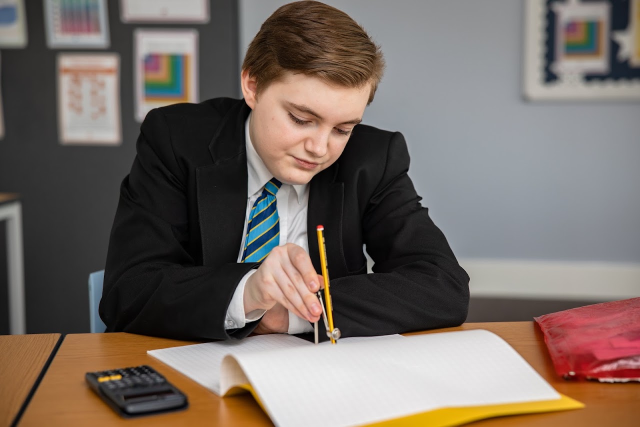 A student at a desk using a compass